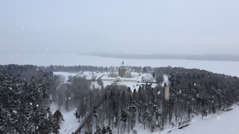 Snow-covered-Pazaislis-Monastery-during-snowfall,-aerial-flying-towards-view