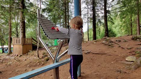 Young-blonde-girl-playing-outdoors-xylophone-in-Mikkelparken-theme-park-Norway---Other-people-passing-in-background