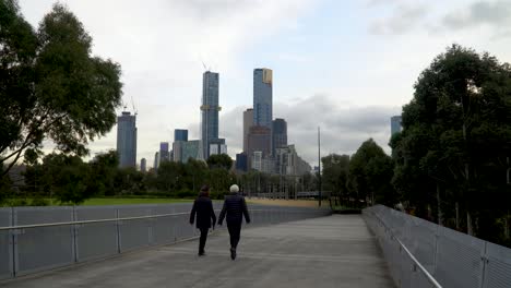 A-couple-walk-down-a-Melbourne-walkway-with-the-skyline-in-the-background---exercise-during-the-coronavirus-lockdown