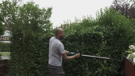 UK-Asian-Adult-Bald-Male-Using-Electric-Hedge-Trimmer-Outside