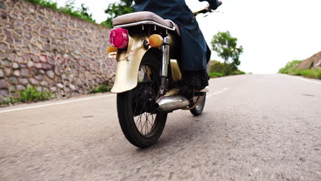 Woman-riding-vintage-motorbike-through-street-with-low-traffic,-close-up-low-angle-view