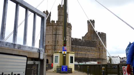 Tourist-walking-on-historic-Caernarfon-castle-swinging-river-bridge-town-landmark