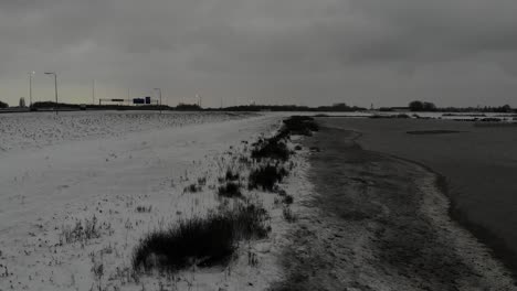 Ruhige-Landschaft-Mit-Schneebedecktem-Flussufer-In-Der-Nähe-Der-Landstraße