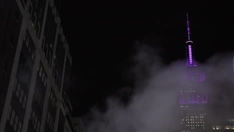 Das-Empire-State-Building-Leuchtete-Nachts-Violett,-Und-über-Den-Rahmen-Dampfte-Kondensationswolke