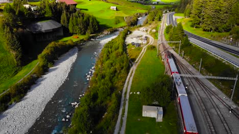 Aerial:-valley,-red-train-and-road-in-the-swiss-alps