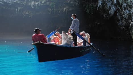 Lago-Y-Cueva-Melissani-En-Kefalonia,-Grecia---Barquero-Y-Turistas-Que-Usan-Mascarilla-Mientras-Están-En-Un-Bote-Flotando-En-El-Agua-Clara-Del-Lago