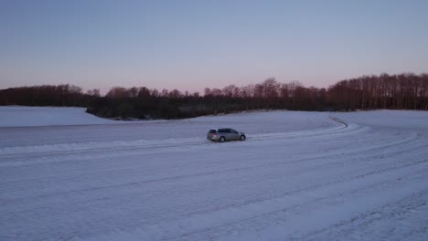Drone-following-vehicle-driving-on-snowy-ice-road-exploring-local-landscapes-in-winter