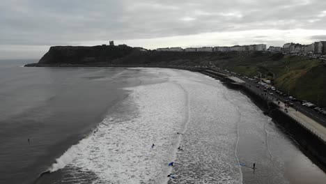 Drone-footage-of-surfers-paddling-out-to-ride-waves-in-Scarborough,-North-Yorkshire,-UK