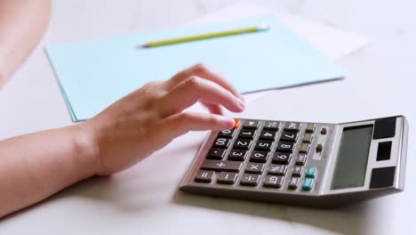 Closeup-hand-of-a-woman-is-using-a-calculator-to-calculate-and-write-down-her-monthly-accounting-expenses-at-home