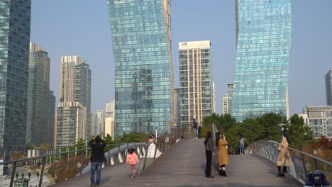 Amidst-a-global-pandemic-and-wearing-face-masks,-Koreans-cross-the-foot-bridge-to-visit-Central-Park-in-Incheon,-South-Korea