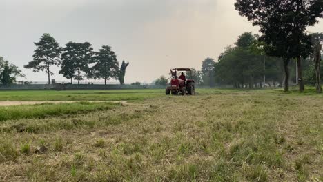 Front-view-of-a-farmer-on-a-red-tractor-plowing-the-green-field-for-making-golf-course