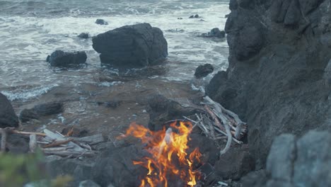 Fire-burning-on-rocky-seaside-shoreline.-Ascending-Shot