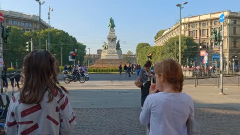Two-children-walking-at-Largo-Cairoli-in-Milan-with-Garibaldi-equestrian-statue-in-background-Italy
