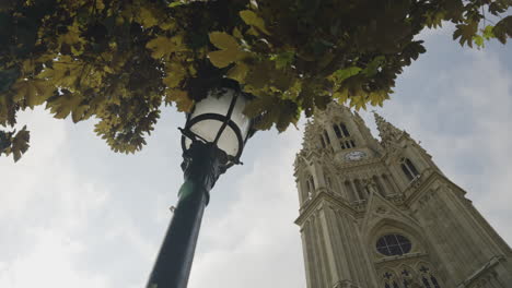 Light-pole,-tree-leaves-and-majestic-church-tower-with-clock-in-San-Sebastian,-motion-view