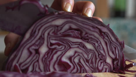 Extreme-close-up-woman's-hand-ends-slicing-part-of-purple-red-cabbage-with-a-sharp-knife-in-the-kitchen