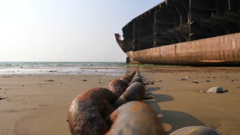 Rusty-Anchor-Chain-Laid-Out-On-Beach-Connected-To-Dismantled-Ship