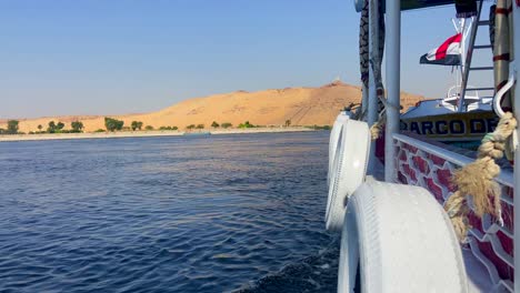 Sailing-boat-with-Egyptian-flag-navigating-through-Nile-river-in-a-sunny-day-with-the-views-of-a-desert