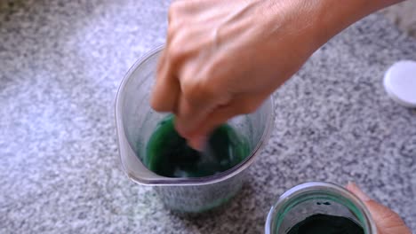 Adding-And-Stirring-A-Small-Spoonful-Of-Spirulina-Powder-To-Green-Juice-In-A-Pitcher
