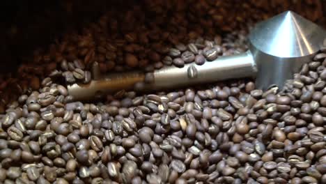 Coffee-bean-roaster-mixing-and-turning-the-grains-with-steel-arms,-Handheld-close-up-shot