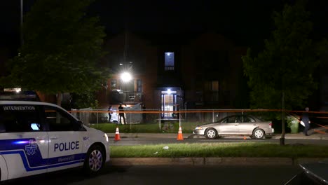 Montreal-police-car-outside-of-apartment-complex-at-night,-police-investigate-scene-in-background