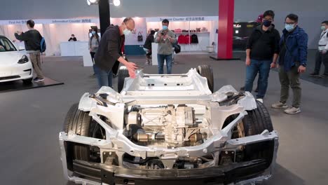 Visitors-look-and-take-photos-of-a-Tesla-Motor-chassis-car-and-vehicle-frame-of-a-motor-vehicle,-during-the-International-Motor-Expo-showcasing-EV-electric-cars-in-Hong-Kong