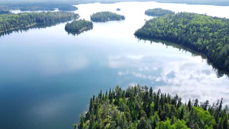 Aerial-footage-of-a-lake-with-the-sky's-reflection-and-lots-of-green-bush-and-trees
