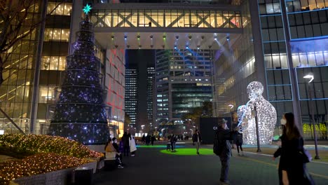 Lotte-World-Tower-Weihnachtsbaum-Und-Menschen,-Die-In-Schützenden-Gesichtsmasken-Spazieren-Gehen-Und-Am-Silvesterabend-Nachts-Fotos-Machen