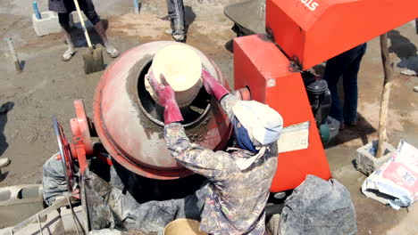 Construction-project-in-Nigeria,-West-Africa-as-workers-mix-cement-carrying-buckets-on-their-heads