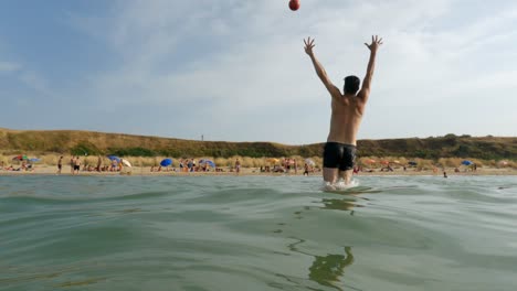 Slow-motion-low-angle-pov-of-goalkeeper-trying-to-save-ball-kicked-from-beach-jumping-in-sea-water,-Punta-Penna-in-Italy
