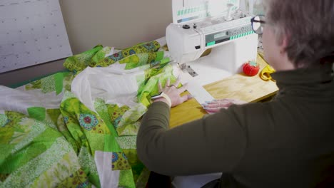 Over-the-shoulder-view-of-a-senior-woman-sewing-the-border-on-assembled-quilt-blocks-to-complete-the-pattern