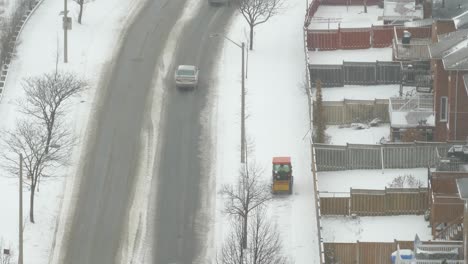 Aerial-shot-of-commuters-making-their-way-to-work-along-a-slippery-and-dangerous-road-during-a-snowstorm,-as-a-government-contractor-plows-the-sidewalk-of-the-neighborhood,-Mississauga,-Canada