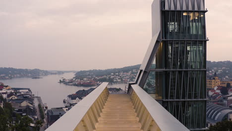 Flying-Over-Empty-Viewpoint-Towards-Glass-Lift-Overlooking-Arendal-Town-Houses-And-Church-In-Norway