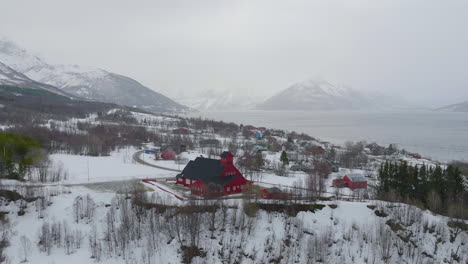 Red-Wooden-Church-In-Kåfjord-Town,-Olderdalen,-Norway-During-Winter---aerial-drone-shot