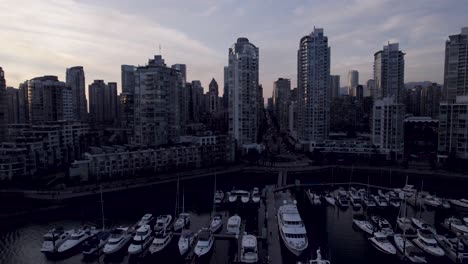 Boats-moored-in-Vancouver-touristic-port-with-skyscrapers-in-background-at-dusk,-Canada