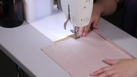Sewing-machine-being-used-to-stitch-entire-side-of-pink-and-white-colored-fabric