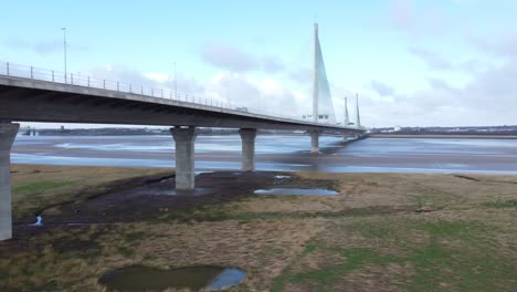 Mersey-gateway-landmark-toll-bridge-at-low-tide-with-river-marshland-aerial-view-descending-low-pan-right