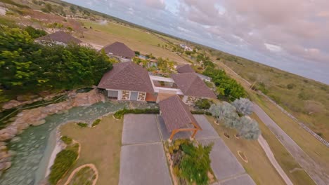 Controlled-drone-flight-at-high-speed-over-Los-Establos,-equestrian-stables-with-green-field-and-sprinkler-in-Cap-Cana,-Dominican-Republic