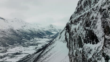 Drohnenschuss,-Der-Entlang-Einer-Vertikalen-Felswand-In-Den-Schneebedeckten-Bergen-Norwegens-Fliegt