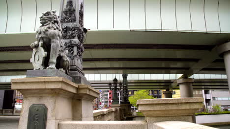 TOKYO,-JAPAN,-circa-April-2020:-pedestrians-walking-on-historical-Nihonbashi-bridge,-stone-carved-lion-sitting-on-the-edge,-at-old-downtown-financial-area-in-central-urban-neighborhood,-evening