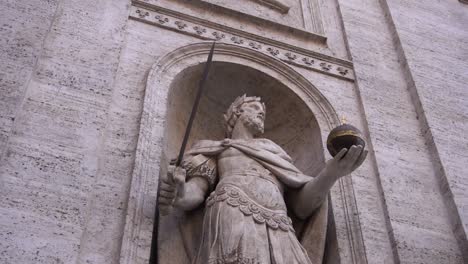 Estatua-De-Un-Emperador-Que-Sostiene-Una-Espada-Y-Una-Reliquia,-Grabada-En-La-Pared-De-Piedra-Blanca-De-Una-Iglesia-Romana