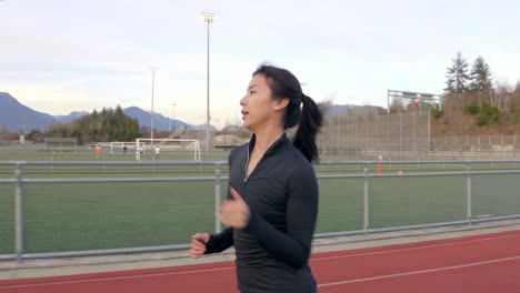 Athletic-young-Asian-woman-running-along-track-outdoors