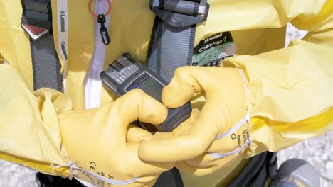 Man-in-yellow-hazmat-suit-checking-chemical-exposure-monitor,-Close-up-shot