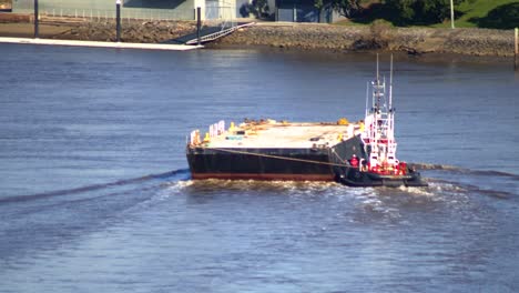 A-tug-boat-manoeuvres-an-empty-flat-deck-barge-down-a-river