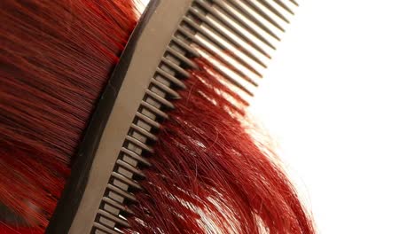 comb-passing-through-curly-red-hair,-close-up-shot