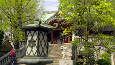 Asakusa,-Tokio,-Japón-Alrededor-De-Abril-De-2020:-Un-Hombre-Dando-Un-Paso-Al-Frente-Para-Adorar-En-Un-Templo-Tradicional-Japonés,-Linternas-Artísticas-En-Un-Tranquilo-Y-Silencioso-Jardín-De-Estilo-Zen-En-Un-Cálido-Y-Soleado-Día-De-Primavera