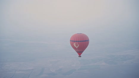 Red-hot-air-balloon-flying-over-landscape-of-Morocco,-handheld-aerial-view