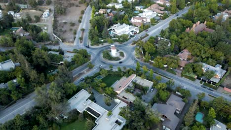 Aerial-dolly-out-rising-over-Leonidas-Montes-windmill-in-roundabout-with-cars-driving-surrounded-by-trees,-Lo-Barnechea,-Santiago,-Chile