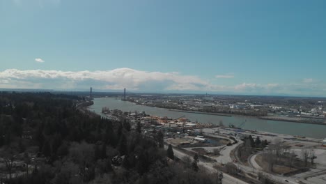 Scenic-view-of-Delta-BC-on-the-edge-of-the-Fraser-river-with-the-Alex-Fraser-bridge-in-the-background-Bright-day-blue-sky-clouds-Aerial-Wide-reversing-revealing-neighbourhood-next-highway