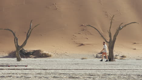 Young-Man-With-Camera-Walking-In-The-Deadvlei,-Clay-Pan-With-Dead-Camelthorn-Trees-Near-Sossusvlei
