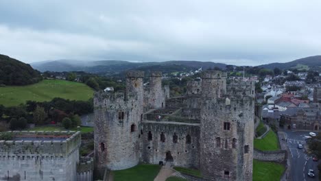 Medieval-Conwy-castle-walled-market-town-aerial-view-rising-over-tourists-walking-battlement-fortification